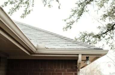 A serene view of a red brick house corner with overhanging tree branches.
